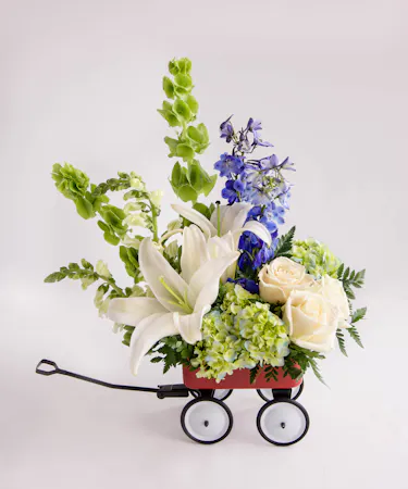 A blue and ivory arrangement designed in a mini keepsake red wagon. 