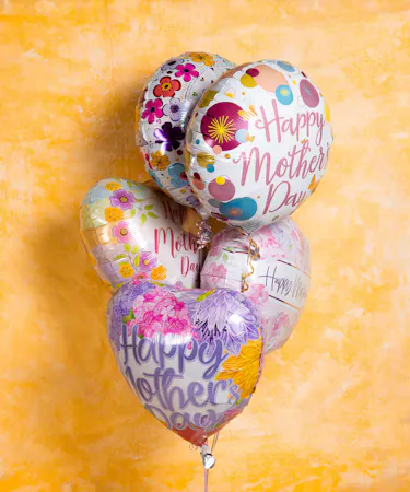 Heart-shaped balloons with floral designs float. One says 