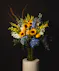A large arrangement of sunflowers, hydrangea, delphinium, and snapdragons in a tall elegant glass vase. 