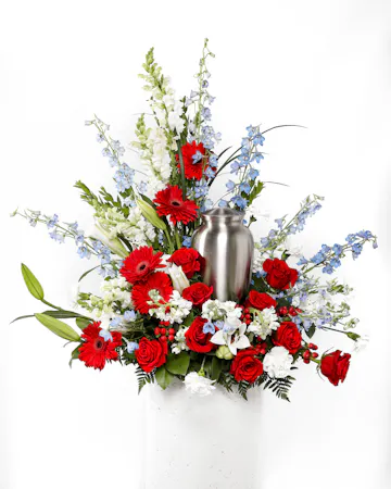 A bold display of vibrant red florals and a touch of blue and white makes the perfect patriotic fireworks display for a cremation urn or photograph.