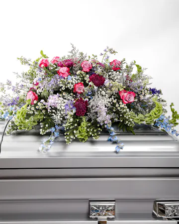 Like a heartfelt embrace, this beautiful casket spray delivers comfort and love in an extraordinary way with lavender and pink florals.