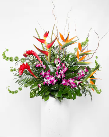 This arrangement of luscious greenery and tropical flowers symbolizes the warmth you have for a loved one you have lost. 