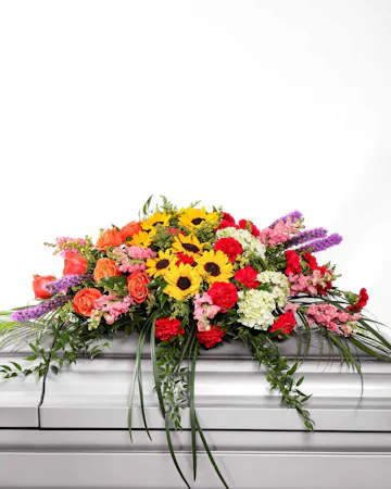 This vibrant and full casket spray is filled with bright blooming flowers.
