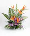 A vibrant floral arrangement featuring orange bird-of-paradise flowers and purple orchids, surrounded by large green leaves, placed on a white surface.