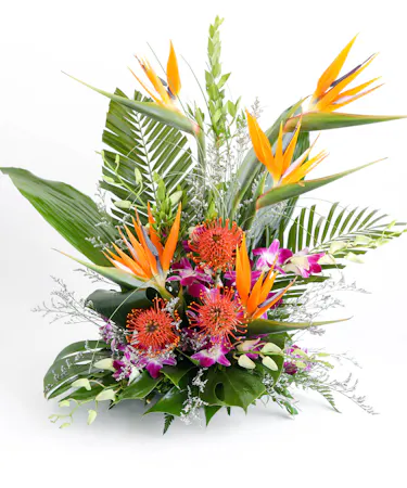 A vibrant floral arrangement featuring orange bird-of-paradise flowers and purple orchids, surrounded by large green leaves, placed on a white surface.