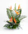 A vibrant floral arrangement featuring orange bird-of-paradise flowers and purple orchids, surrounded by large green leaves, placed on a white surface.