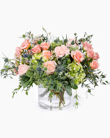 Filled with roses and carnations, This garden-styled arrangement blends the soft hues of peach-colored blooms with the lush greenery of a flourishing garden.