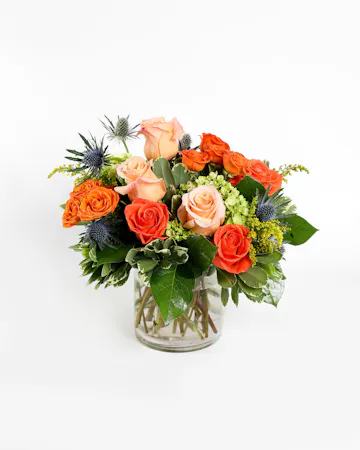 An orange tropical flower arrangement featuring birds of paradise, thistle, and roses. 