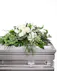 White blooms and a variety of lush greens are artfully arranged to perfectly adorn the top of their casket, offering the colors and ambiance of grace and serenity.