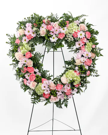 The Graceful Condolence Open Heart is bursting with love and comfort with a mix of pink florals and greenery in the shape of a heart. 