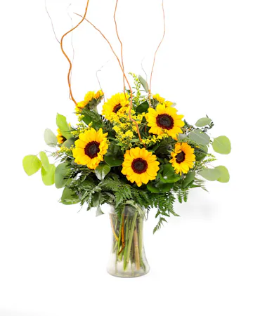 Bright petite sunflowers with cheerful yellow solidago and fresh greenery in a clear, hourglass-shaped glass vase. 