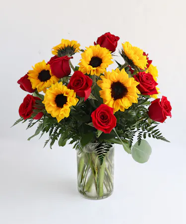 This beautiful display of floral features 9 roses in your choice of pink or red, and 8 dazzling sunflowers arranged with fresh greenery in a tapered glass vase. 